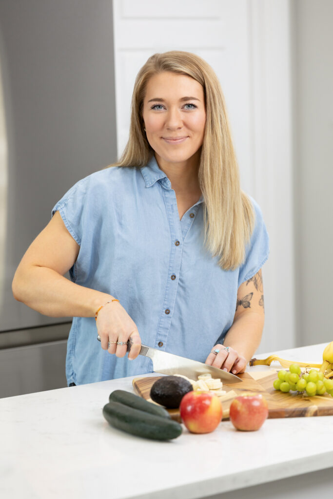 Woman smiling at camera while cutting fruit in a kitchen during a branding photography session in Salt Lake City, Utah.