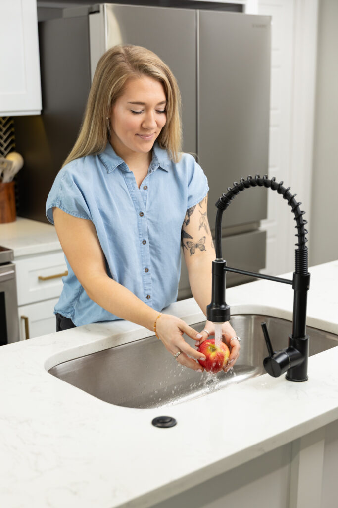 Woman washing an apple in the sink while taking photos during a branding session in Utah with Sara Vaz.