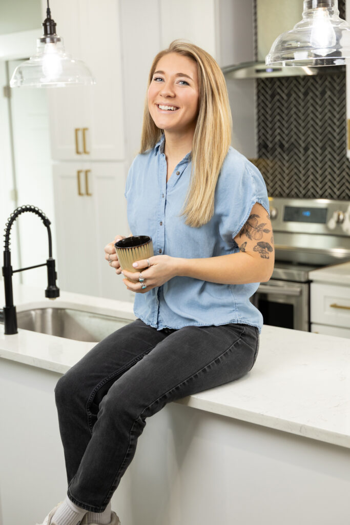 Woman smiling at the camera while shooting a brand session as she sits on the kitchen island.