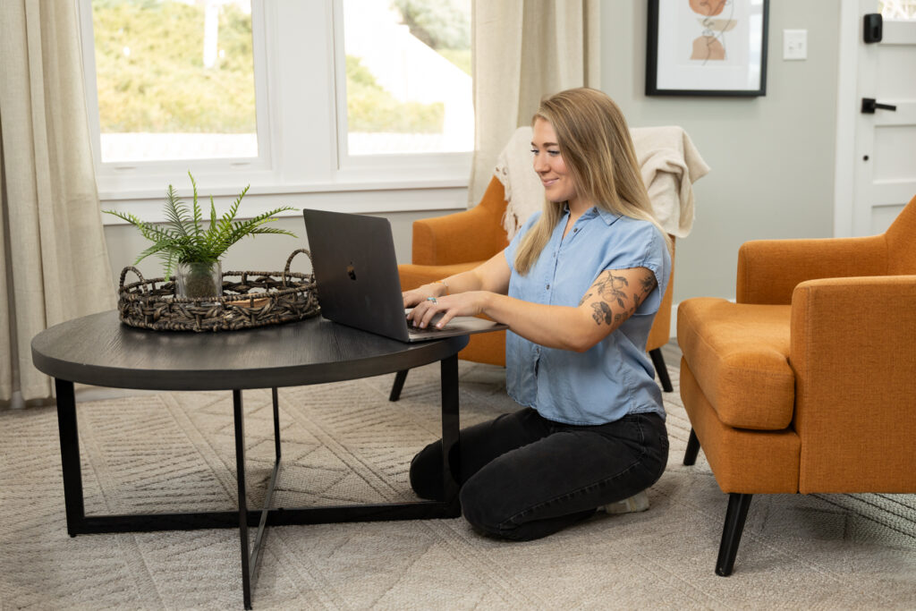 Woman sitting by coffee table while working on her laptop during a brand shoot in Utah.