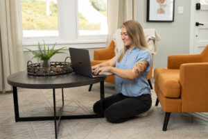 Woman sitting by coffee table while working on her laptop during a brand shoot in Utah.