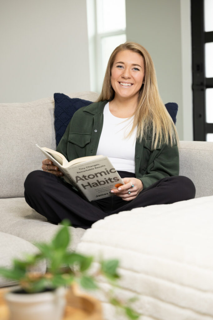 Woman sitting on couch reading book and smiling at the camera during branding session.