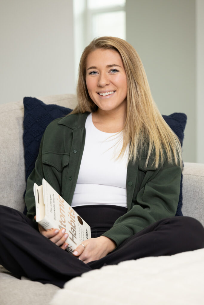 Woman smiling at camera during brand shoot while sitting on the couch with a book.