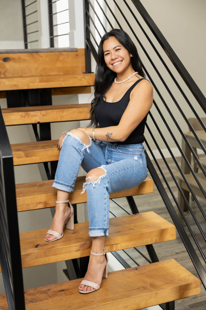 Woman posing on stairs with a black tank, ripped jeans, and high heels for her brand session.